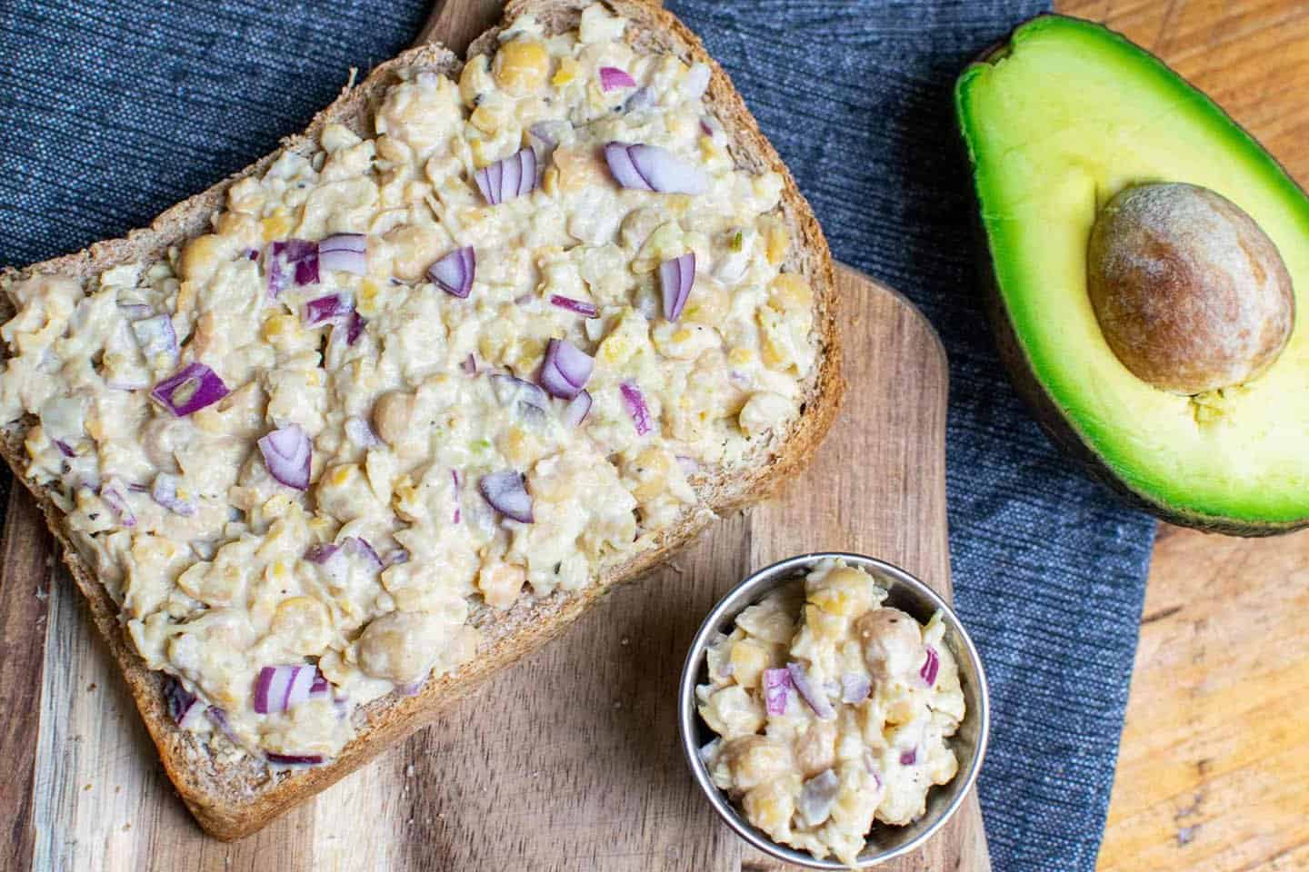 Vegan tuna open sandwich shown on a wooden chopping board , with an avocado in the background to right.