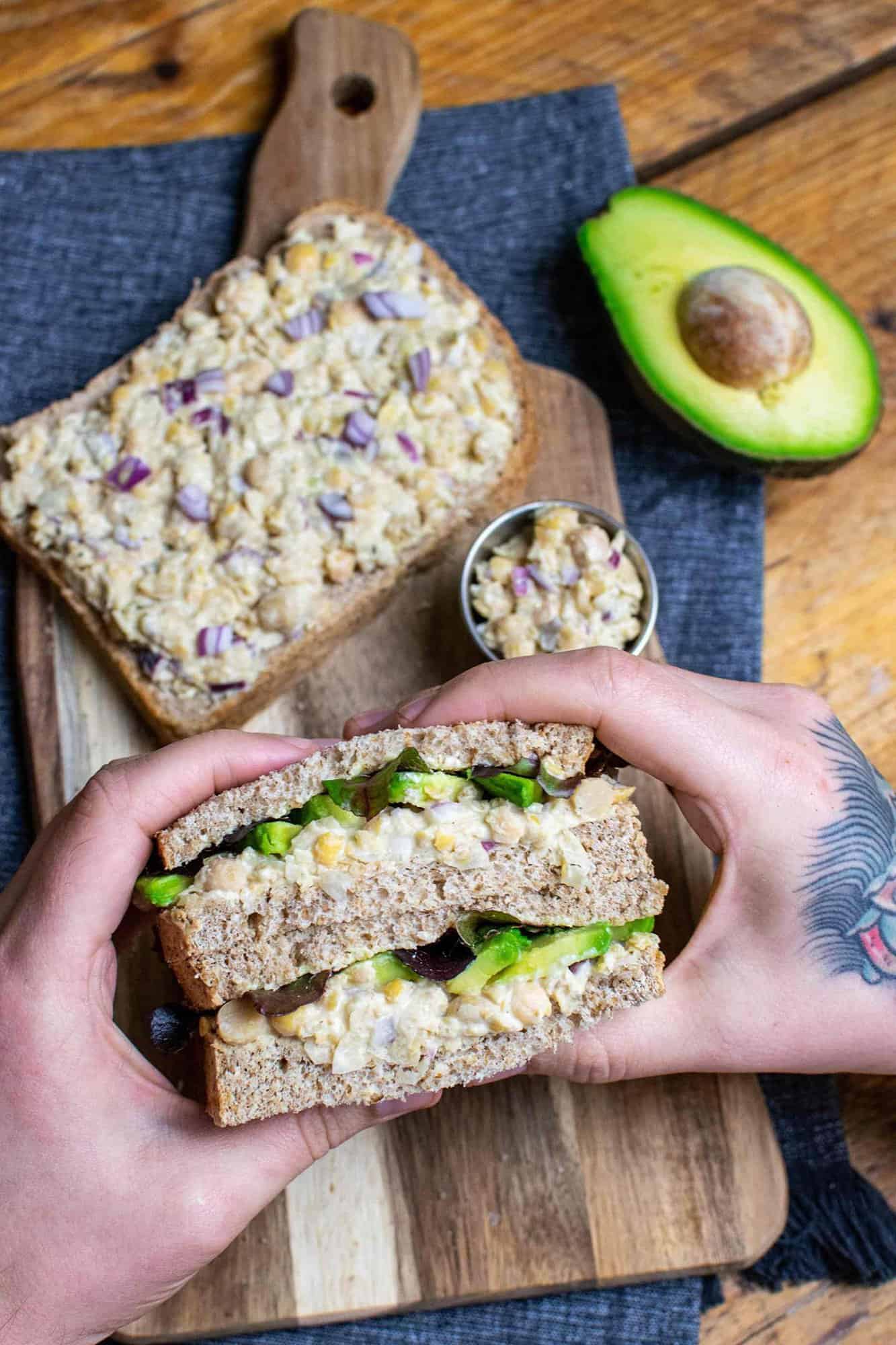 Vegan tuna sandwich being held up by a pair of hands on a chopping board.