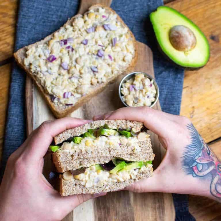 Vegan tuna sandwich being held up by a pair of hands on a chopping board.