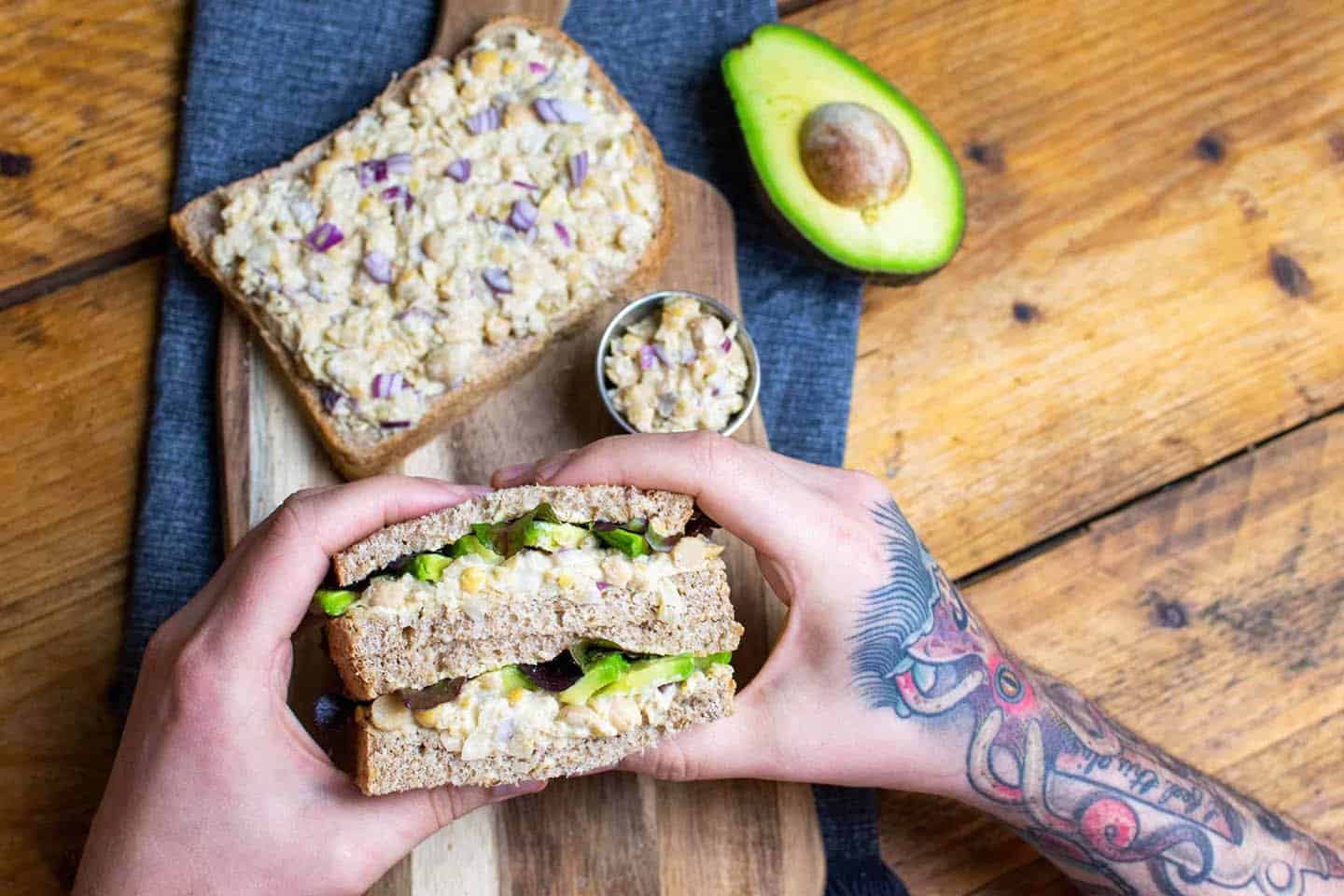 Vegan tuna sandwich being held up by a pair of hands on a chopping board.
