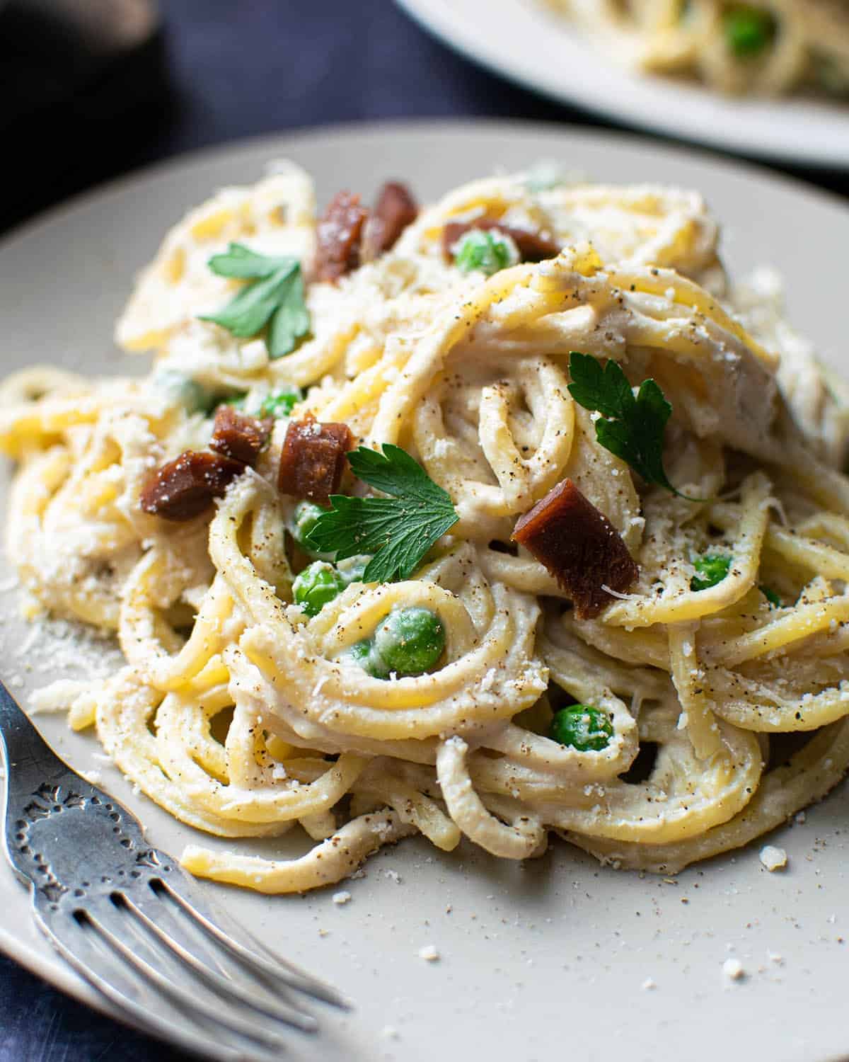 Close up of vegan spaghetti carbonara with a fork and a plate of pasta in the background