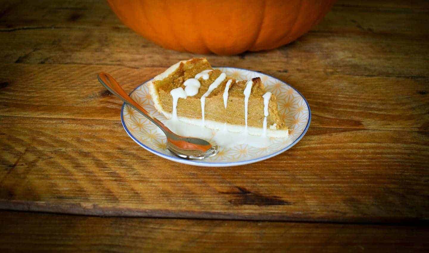 A slice of vegan pumpkin pie on a small plate in front of a pumpkin that can be seen in the background