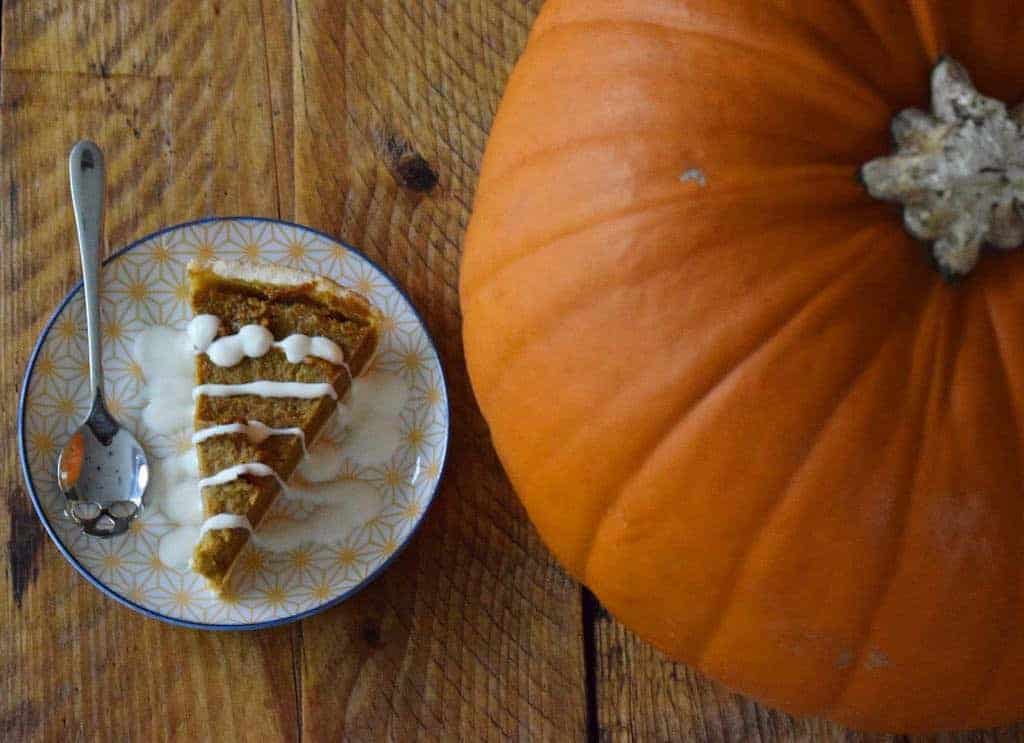 Top down view of a piece of vegan pumpkin pie with a large pumpkin to the right hand side