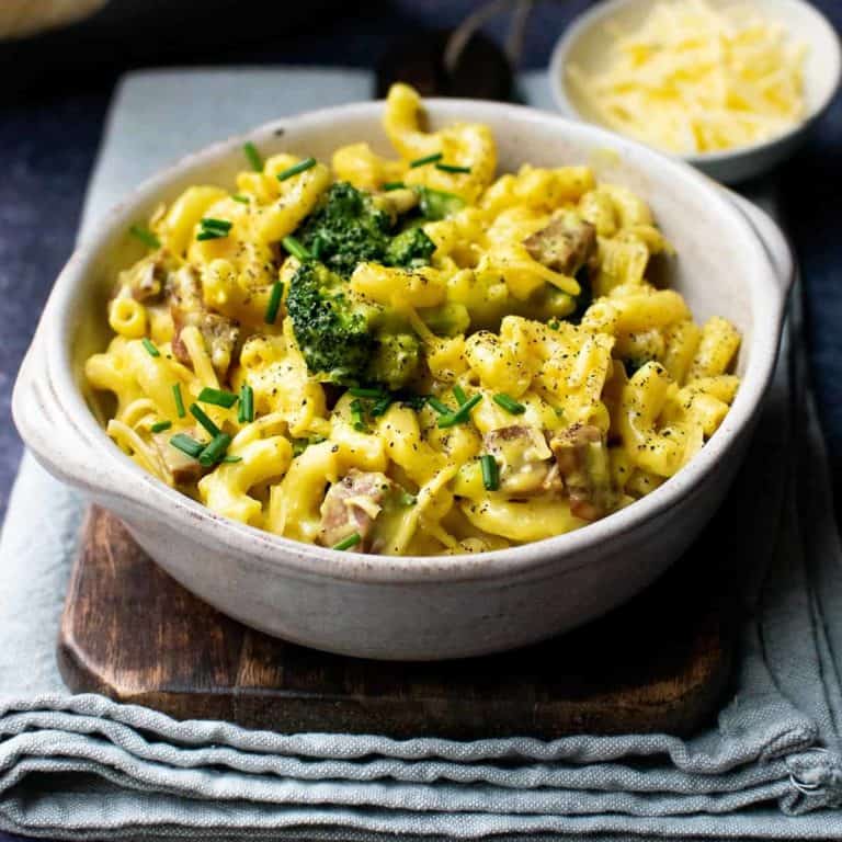 A bowl of vegan mac and cheese with a smaller dish of grated vegan cheese in the background