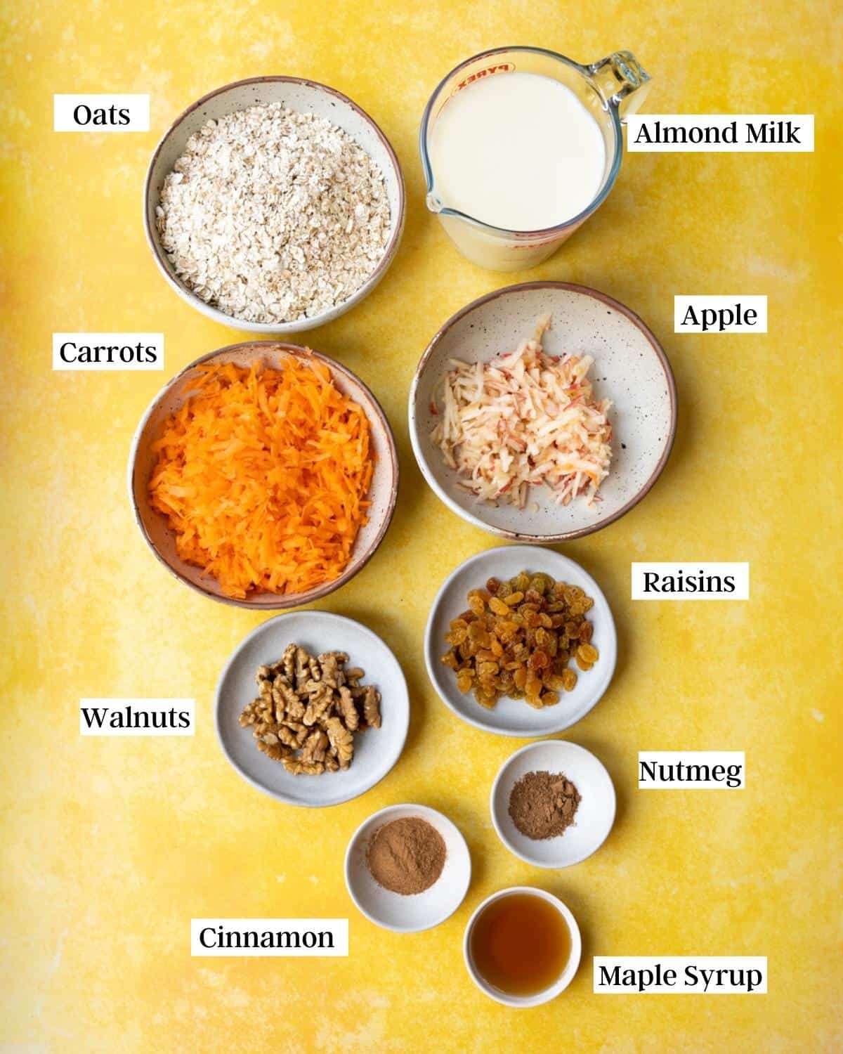 Ingredients for carrot cake porridge laid out in bowls on a yellow surface.