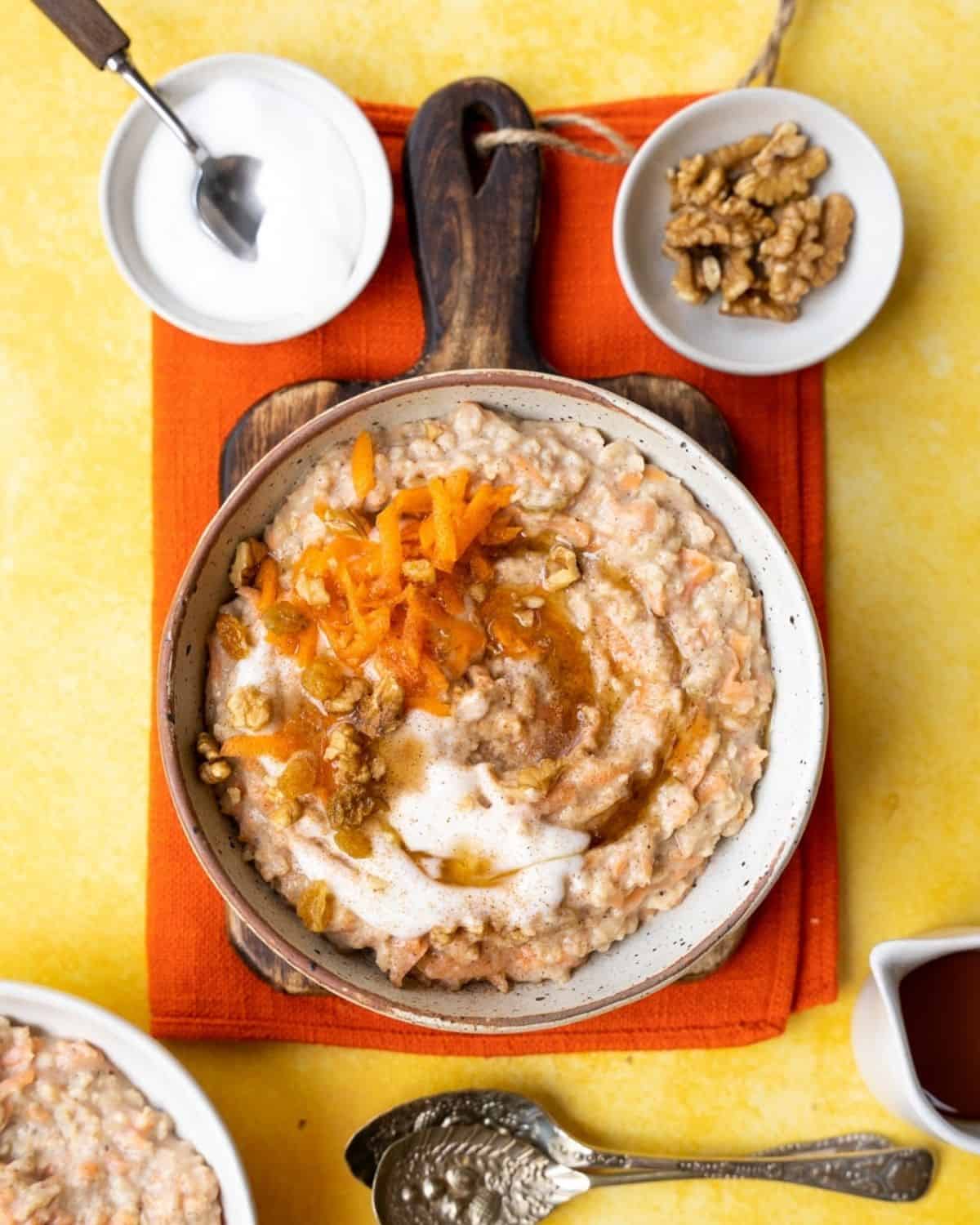 Porridge served with yoghurt, carrots and nuts with spoons.
