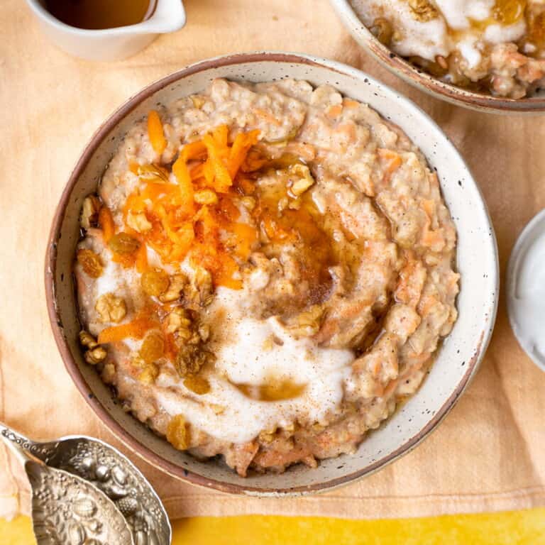 Carrot cake porridge in a bowl topped with yoghurt, walnuts and grated carrot.