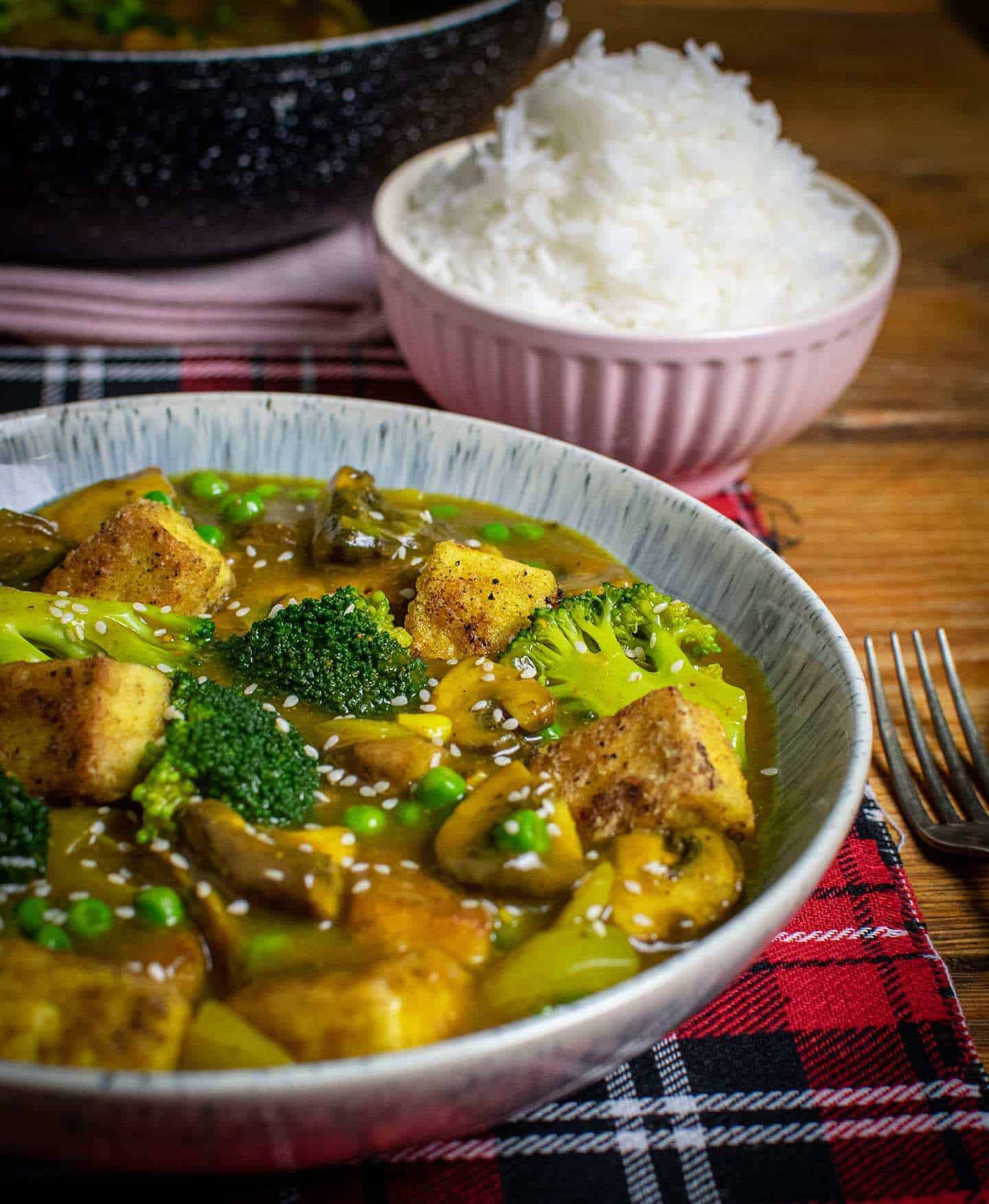 Vegan Chinese curry close up with a pink bowl filled with rice and a wok in the background