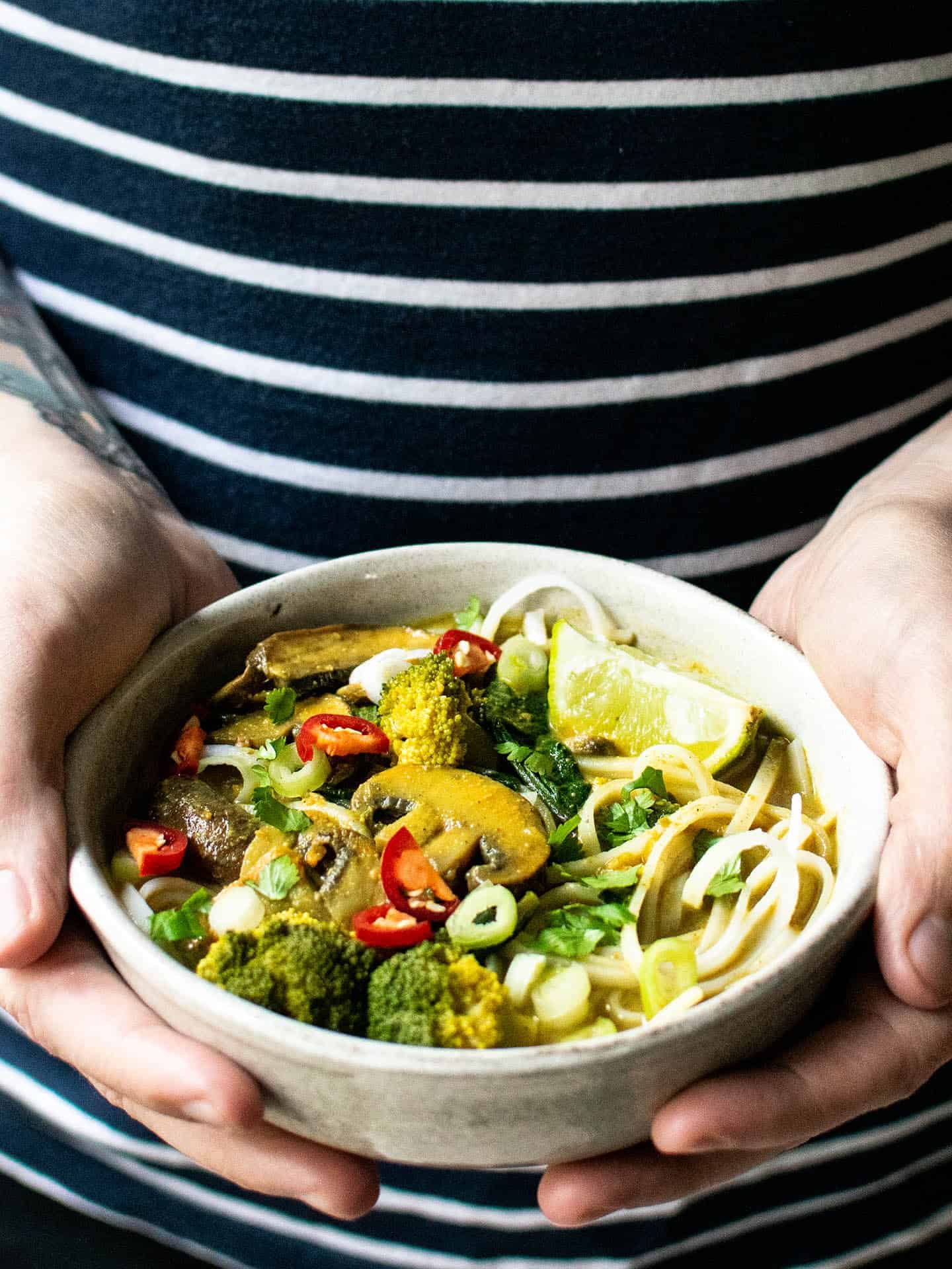 Hands holding a bowl of noodle soup against a stripy t-shirt