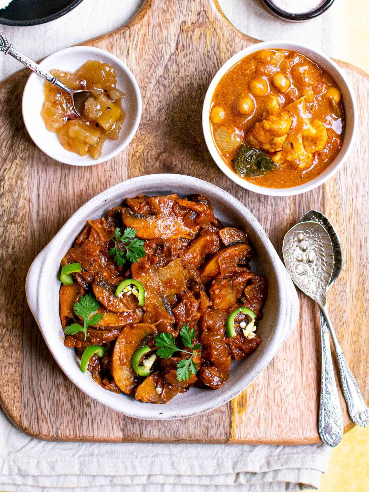 Mushroom bhaji in a white dish with curry and chutney in the background