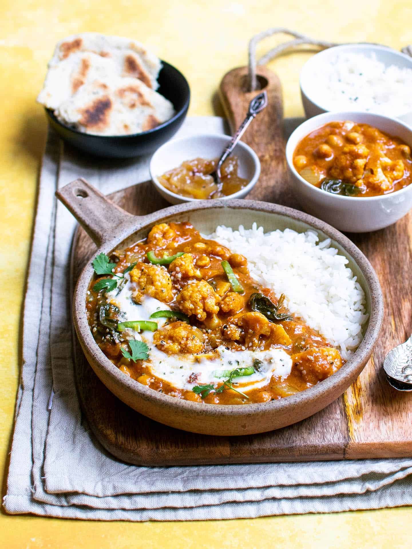 Curry in a bowl with a smaller bowl of curry behind it and chutney and naan bread too