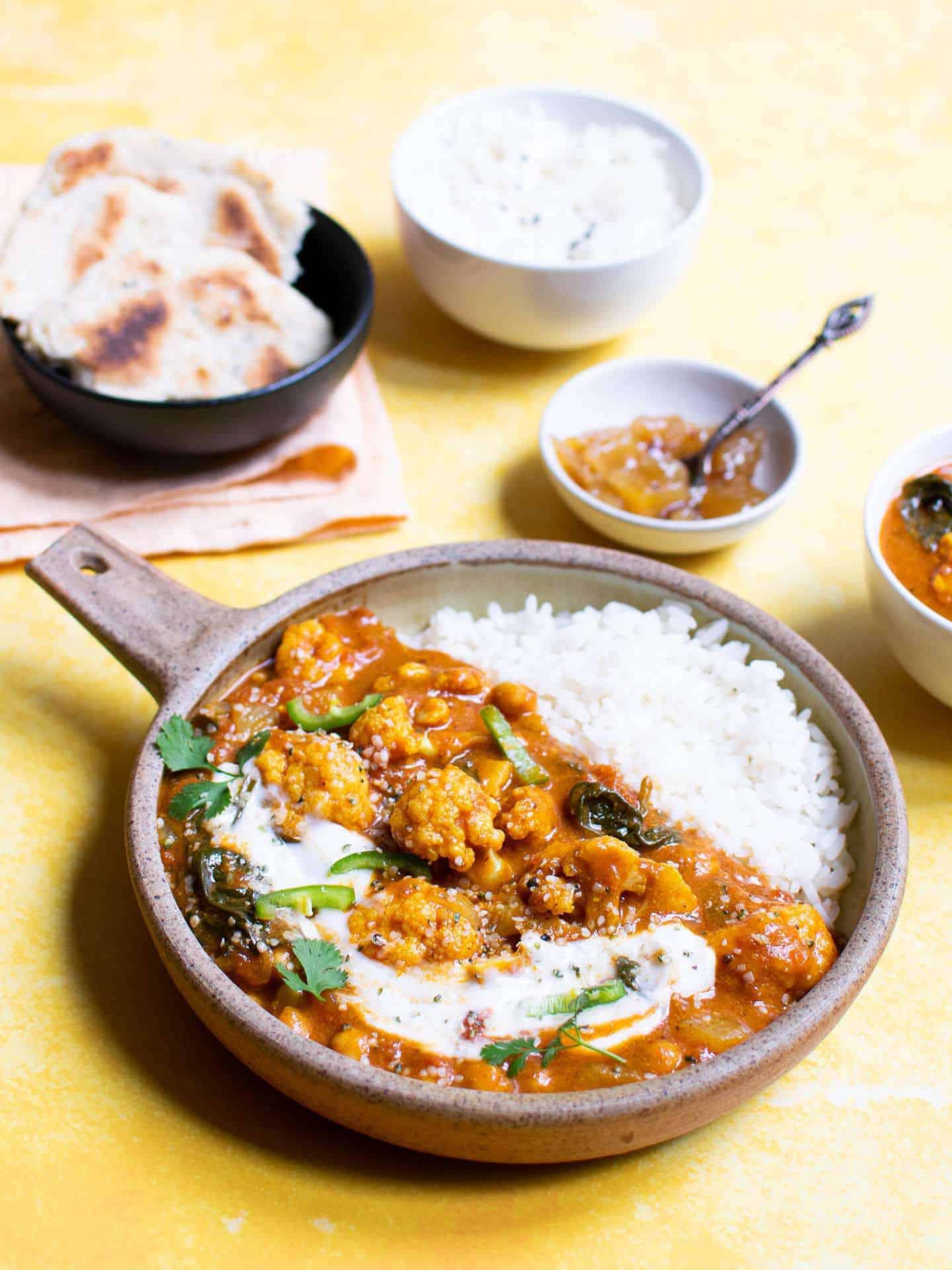 Vegan cauliflower curry in a dish with ingredients including bread in the background