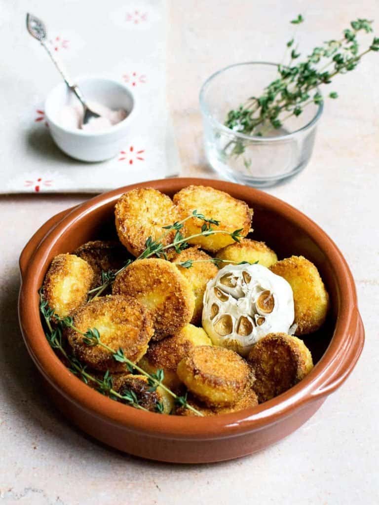 Roast potatoes in a ceramic dish with thyme in the background, set on a light work surface