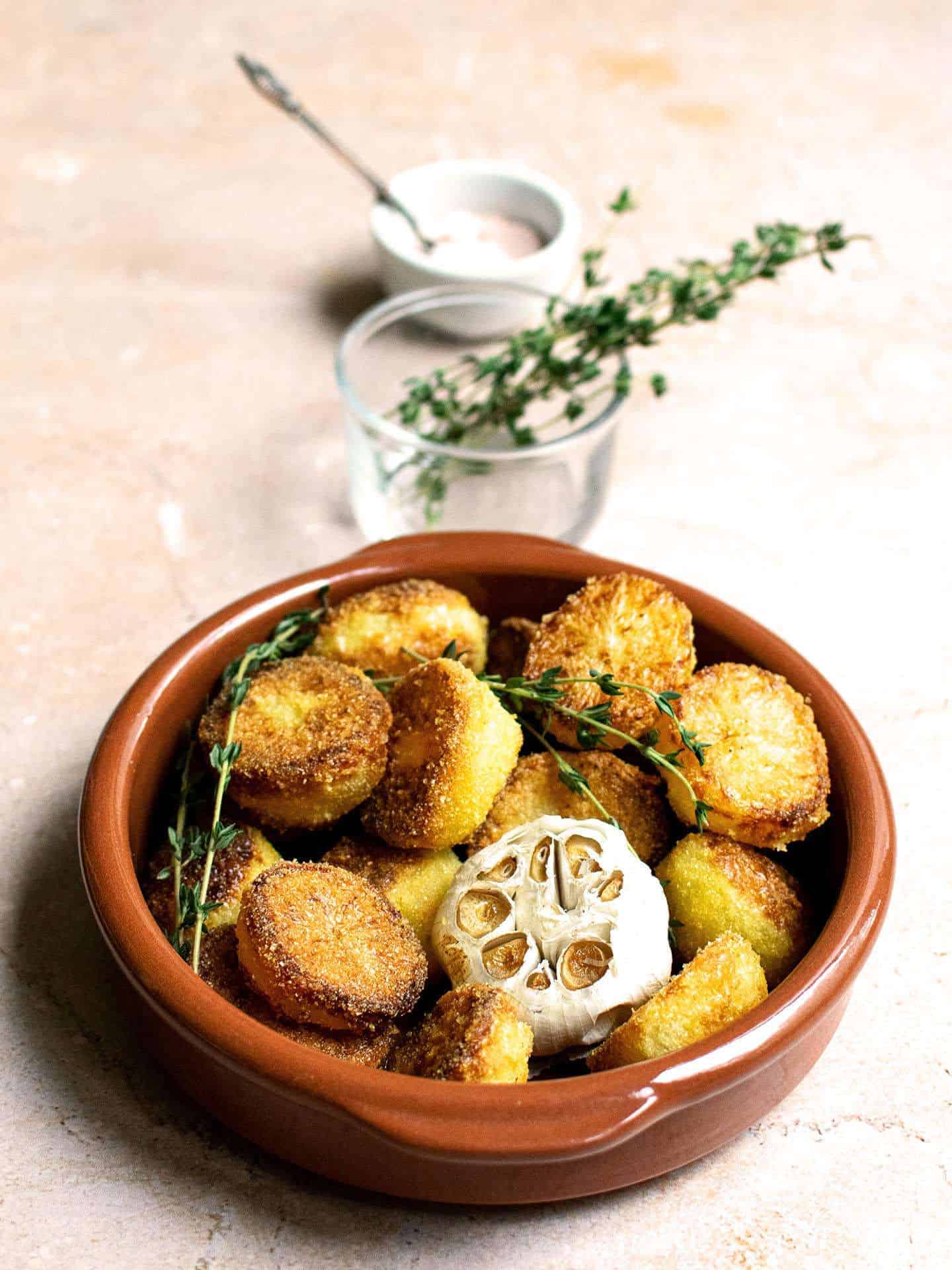 Potatoes with roasted garlic and a pot with thyme in a line behind them, along with a white pot with a spoon in it