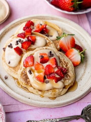 Fluffy vegan pancakes on a plate with yoghurt and strawberries.
