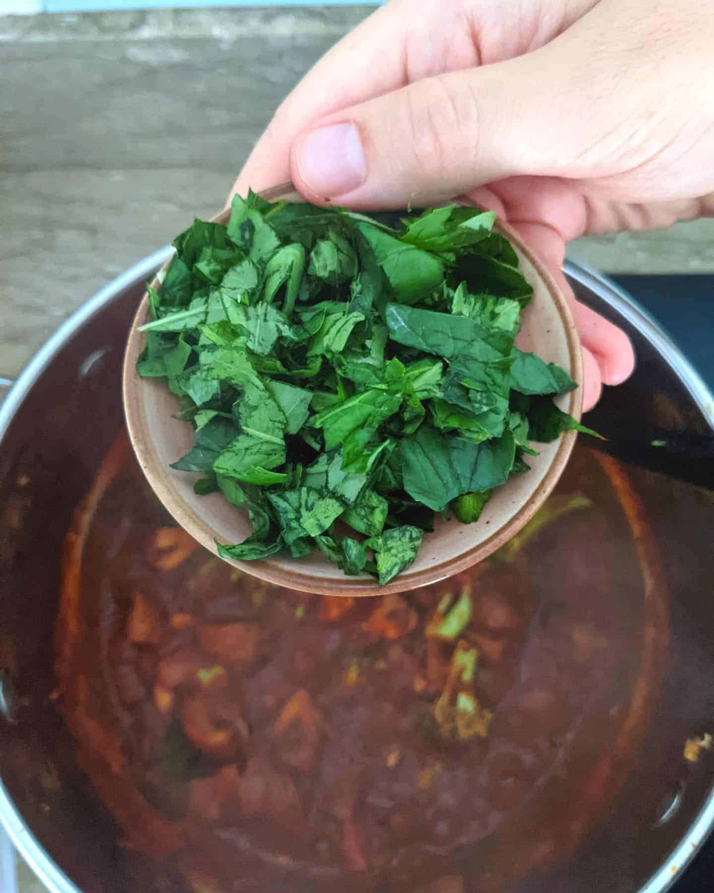 Chopped basil in a small dish about to be poured into a pan of vegan arrabiata sauce