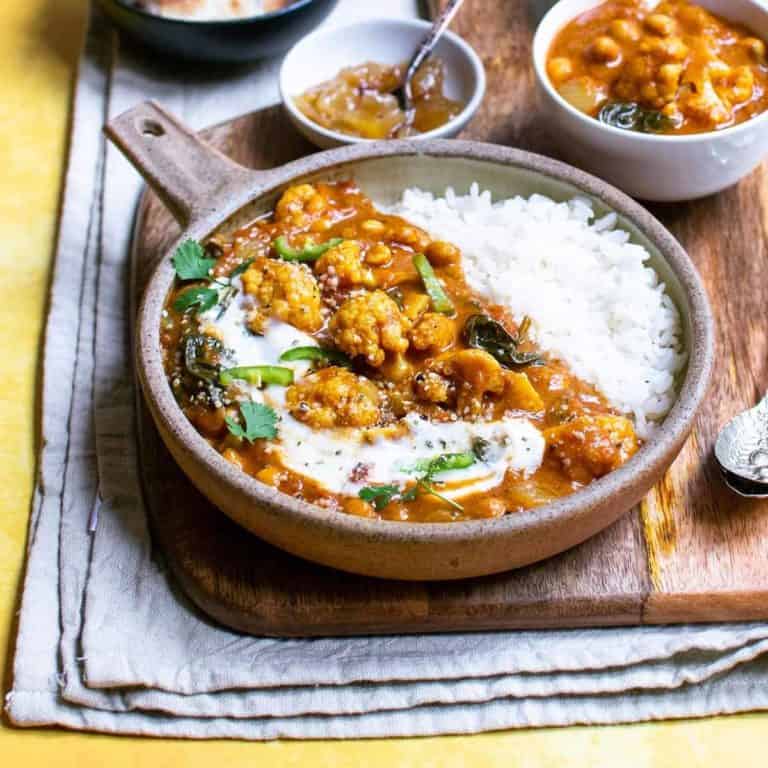 Vegan cauliflower curry in a dish with pinch bowls around it