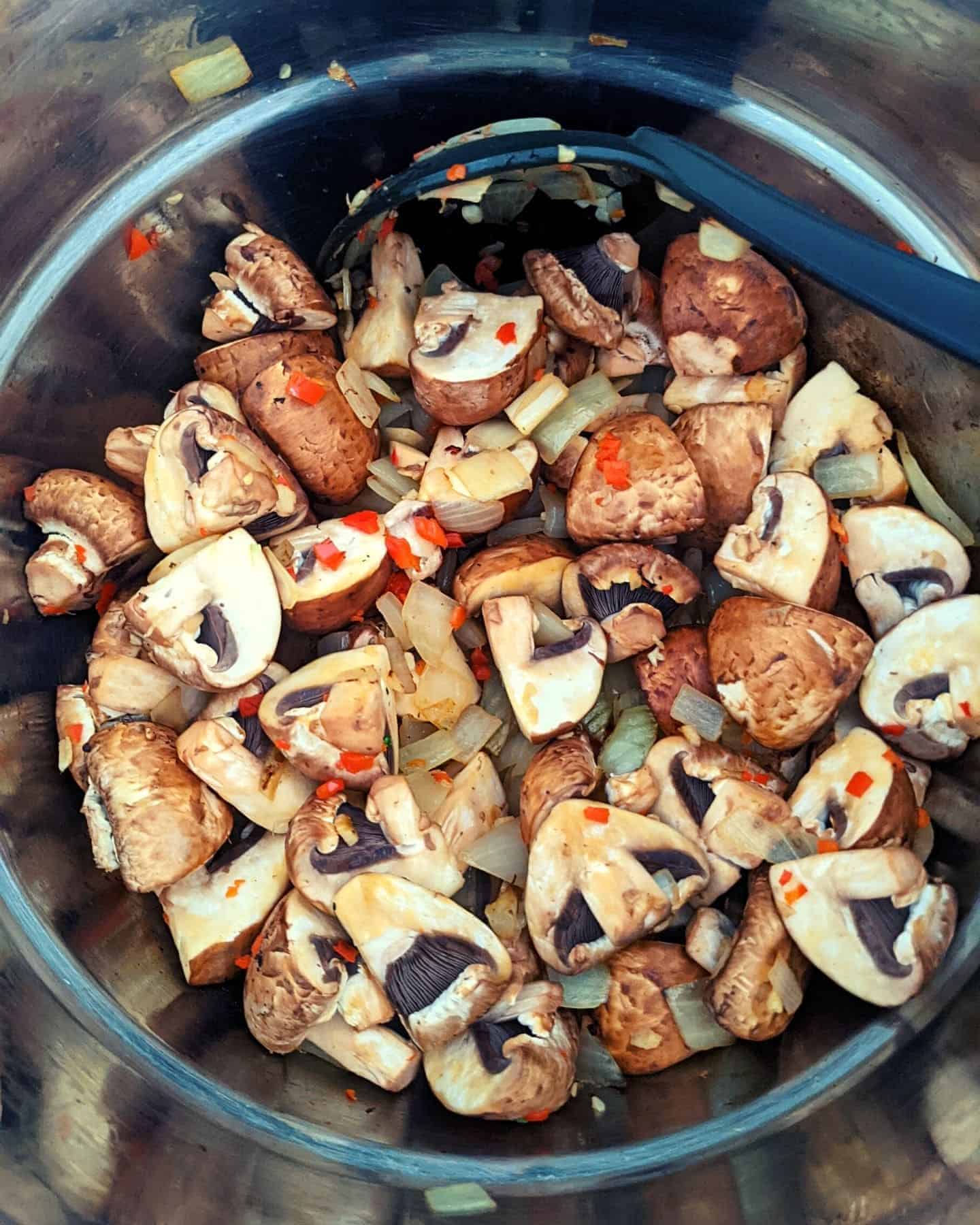 Chopped mushrooms in a deep pan with a black stirring spoon resting against the side