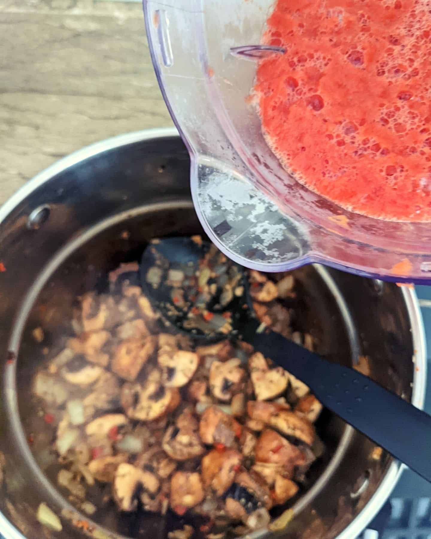 A jug of blended tomatoes about to be poured into a pan