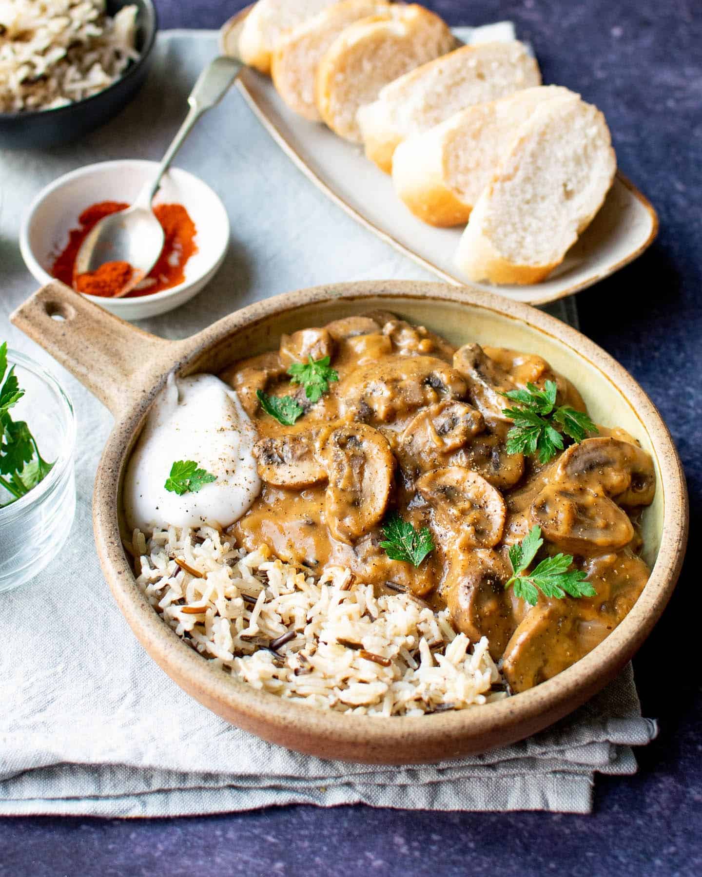 A bowl of stroganoff. It's served with wild rice and there's a plate of crusty bread in the background.