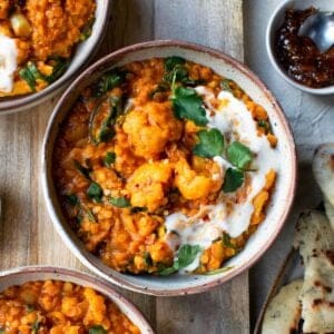 Red lentil curry in a bowl topped with fresh coriander, yoghurt and chutney.