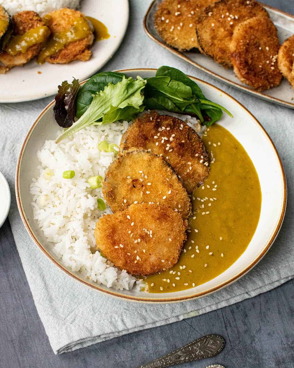 Sweet potato katsu with aubergine, salad and white rice. With more katsu vegetables in the background.