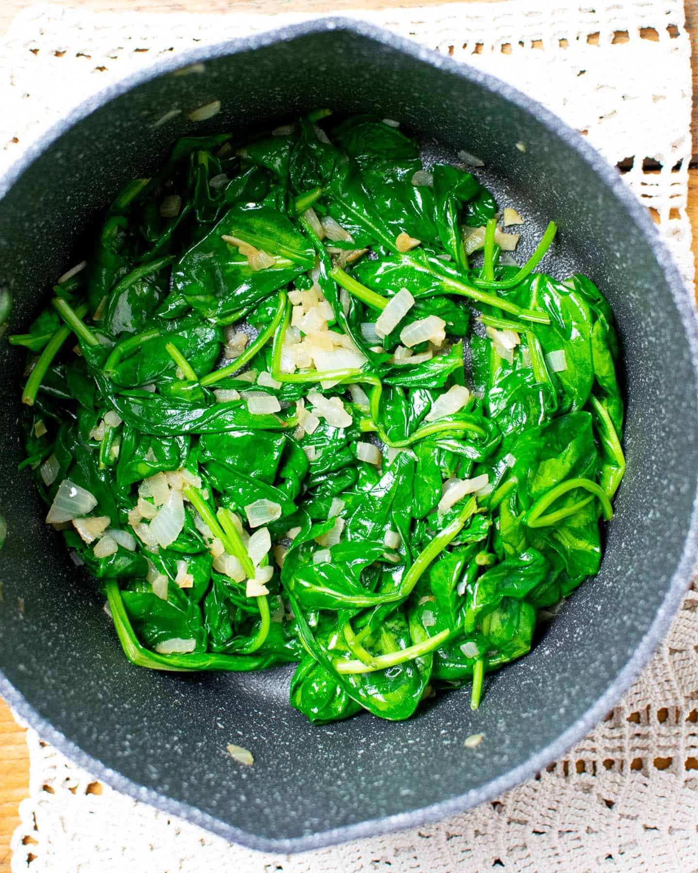 A pan with wilted spinach, fried garlic and onion inside
