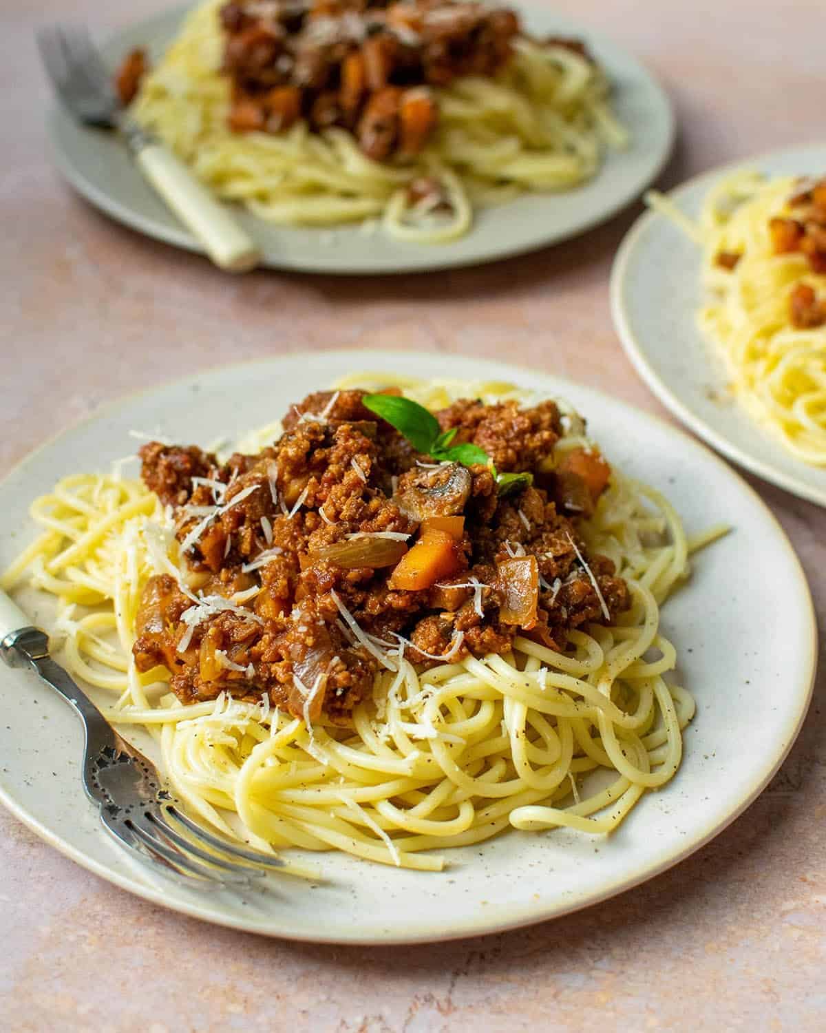 Vegan spaghetti bolognese on a plate with two more plates in the background