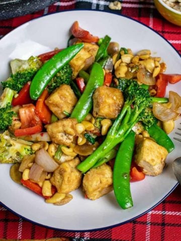 Thai Cashew Stir-fry on a white plate with cutlery balanced on it.