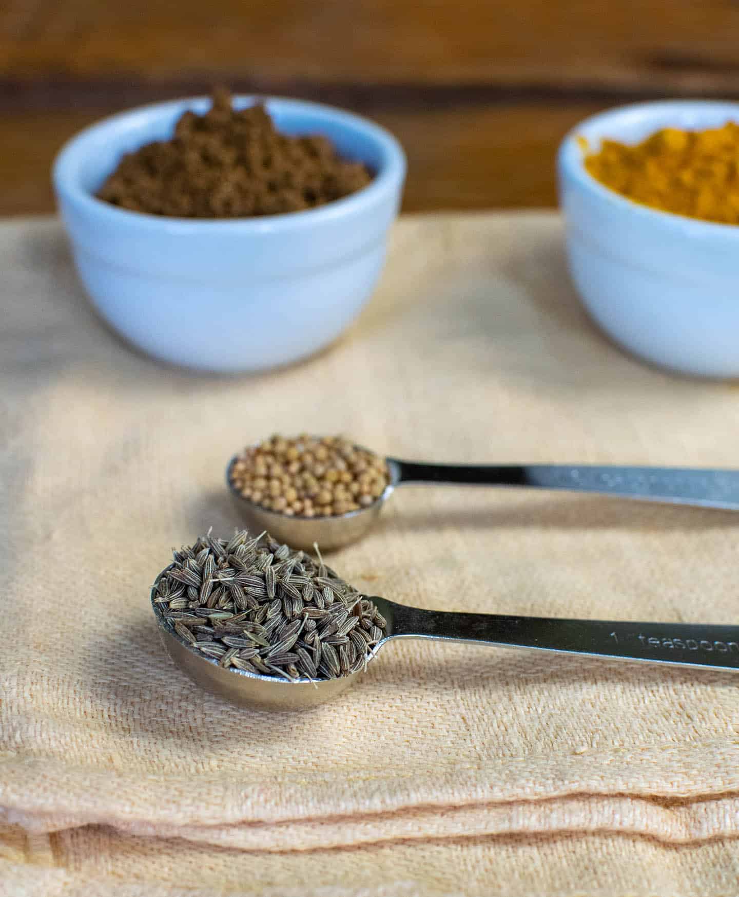 Spices laid out on an orange cloth, showing cumin seeds, garam masala, cumin and turmeric.