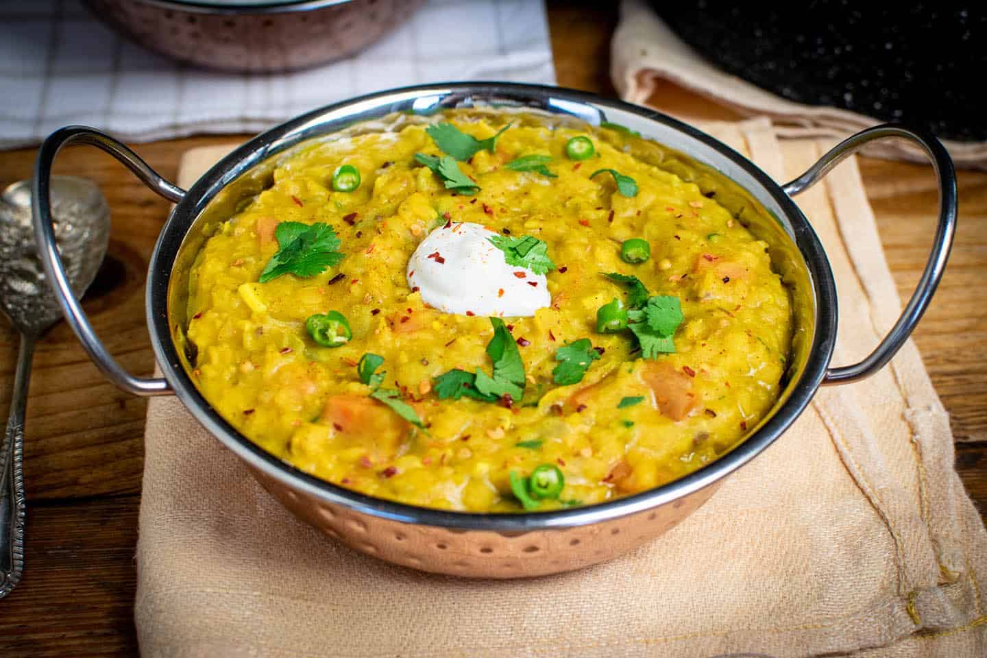 Yellow dahl in bowl topped with coriander, dairy free yoghurt and carrots are visible.