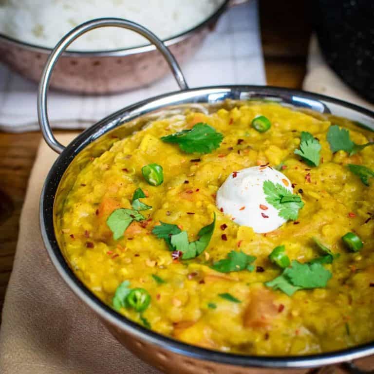 Vegan dahl close up, it's yellow and full to the top in a metalic Indian dish.