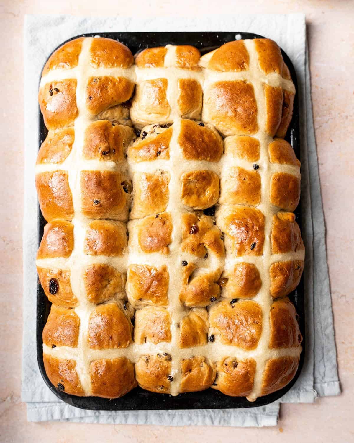 Full tray of vegan hot cross buns fresh out of the oven on a marble surface.