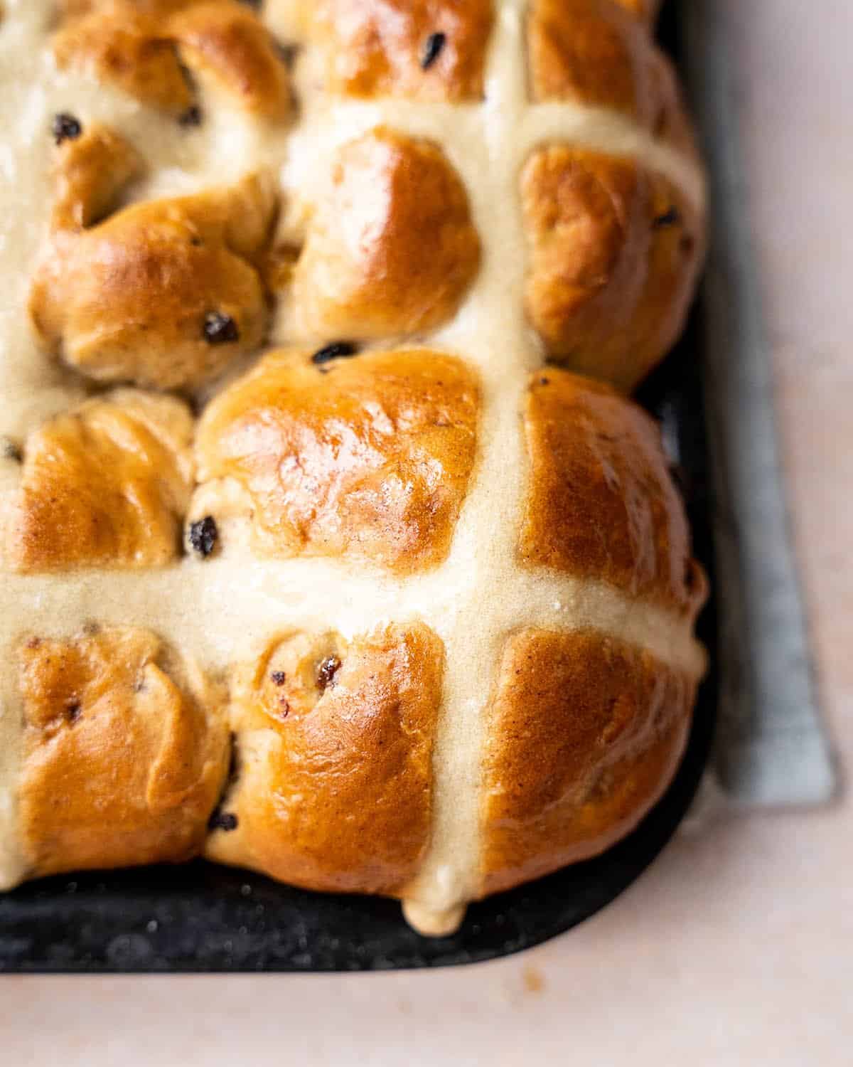 Close up of a vegan hot cross bun in the corner of a full tray of them.
