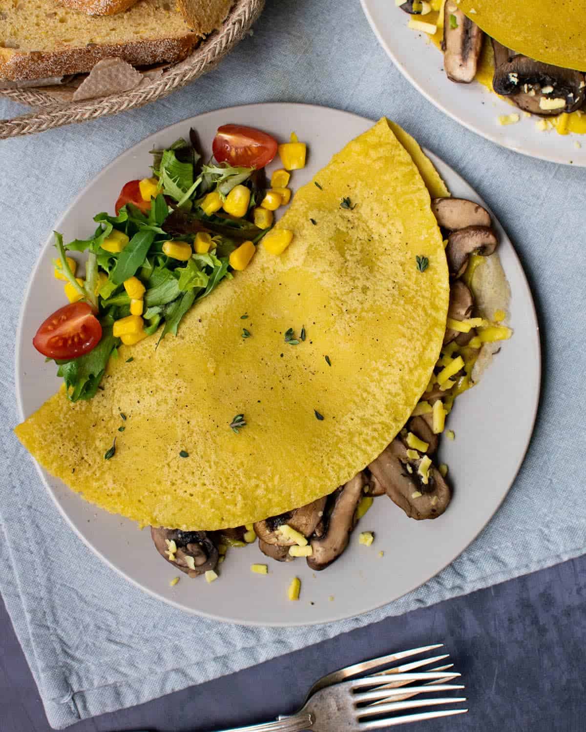 A chickpea flour omelette on a plate filled with mushrooms and served with a side salad.