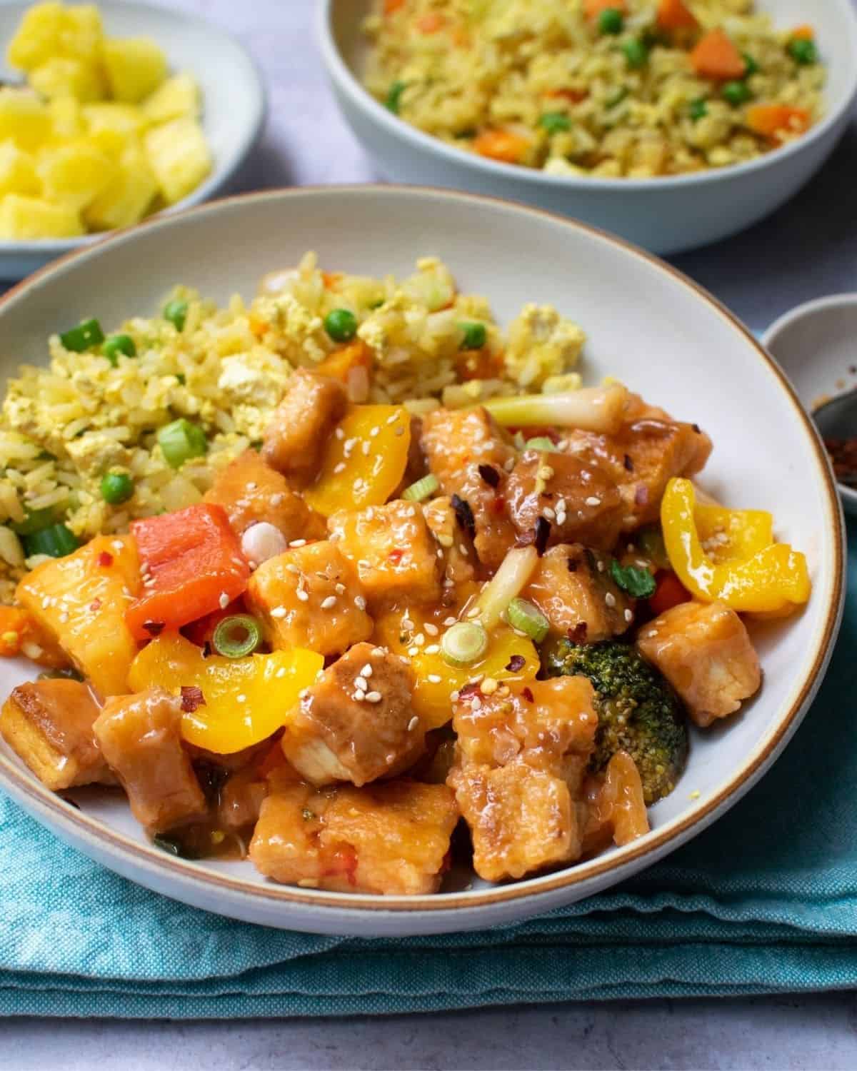 Tofu in vegan sweet and sour sauce served with fried rice. Other bowls visible behind it.