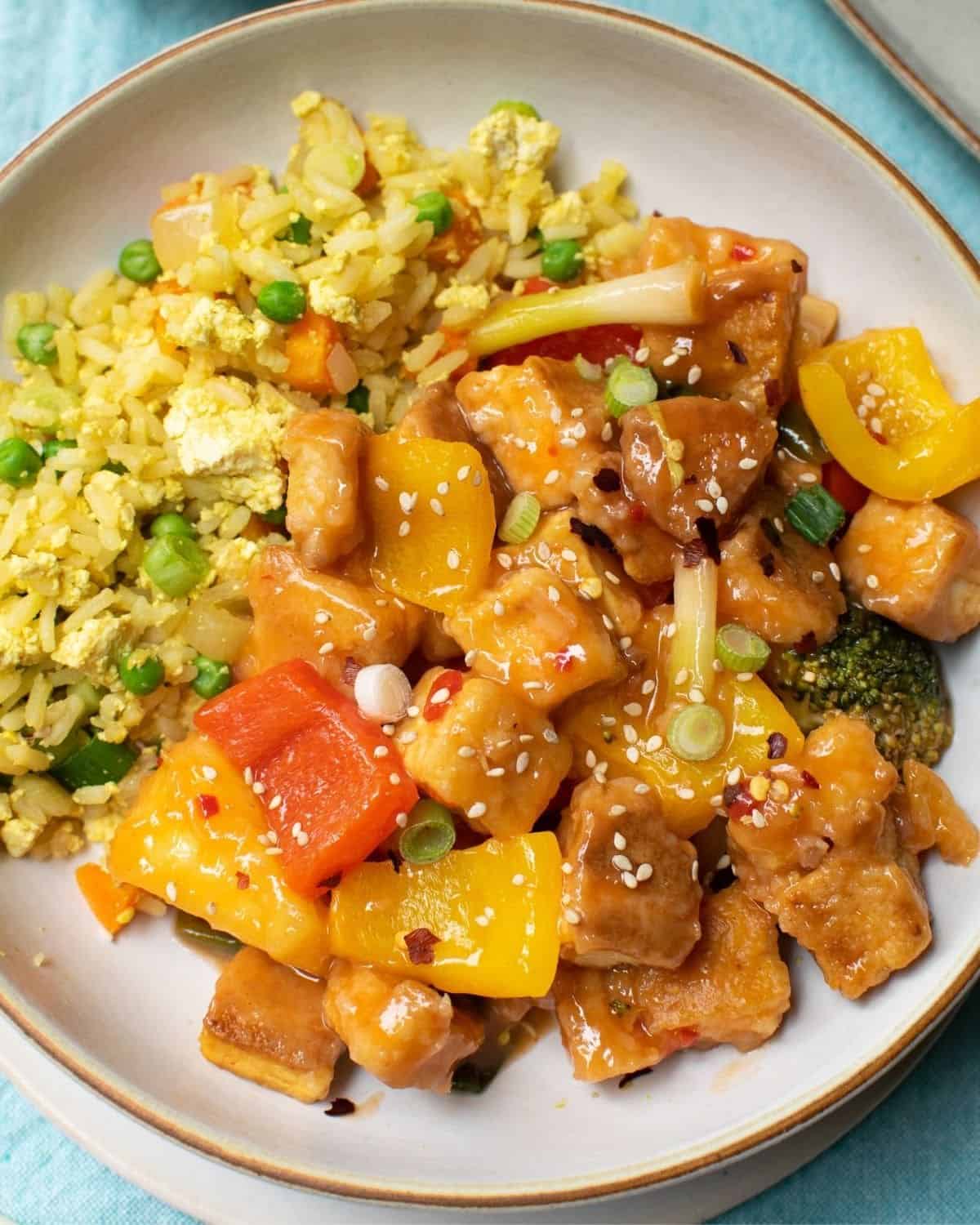White bowl filled with sweet and sour tofu with peppers, broccoli and rice.