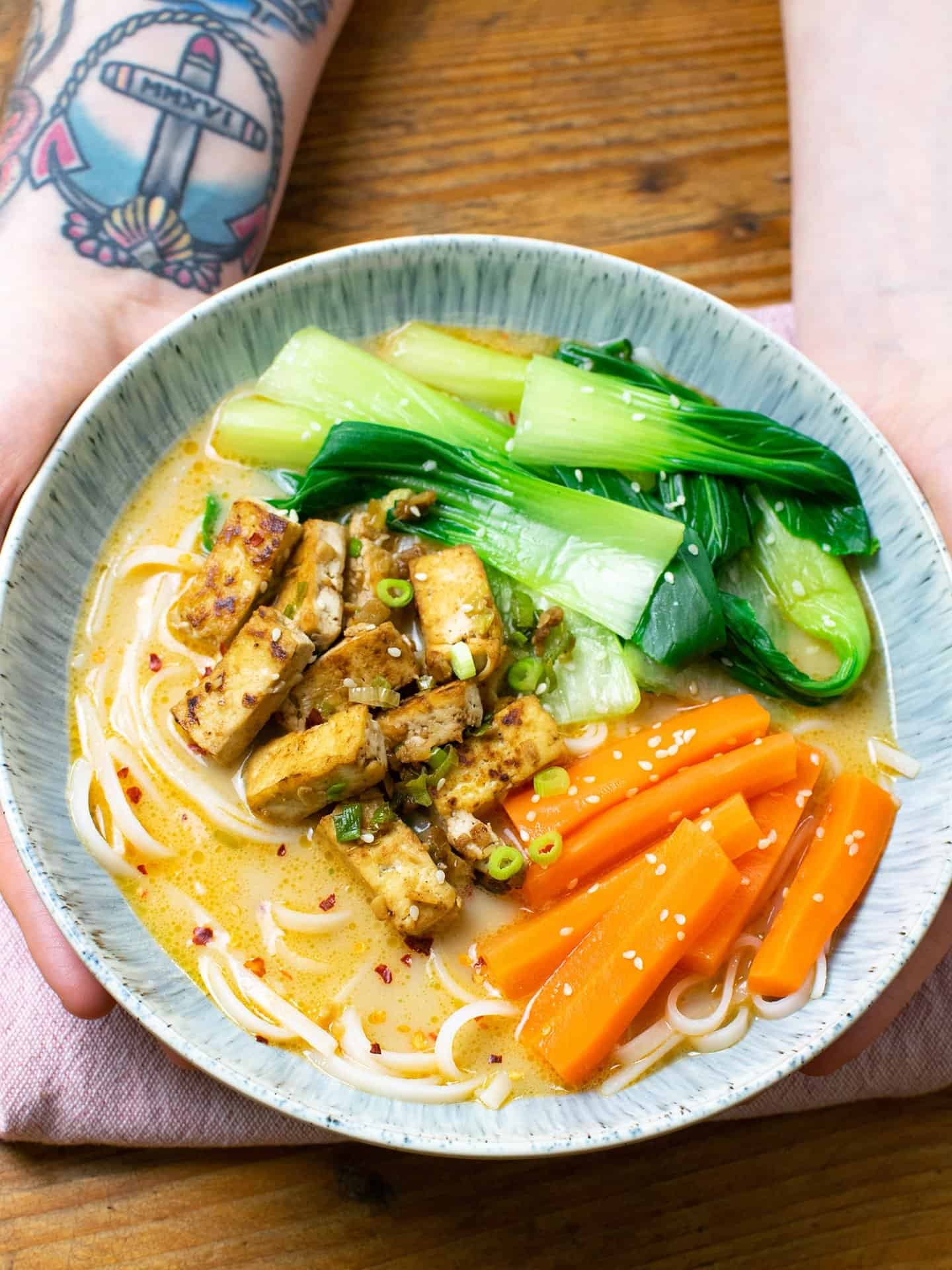 Vegan Tan Tan ramen in a bowl. Noodles, pak choi, carrots and tofu can all be seen, sitting in a delicious golden broth