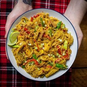 A big plate full of vegan Singapore noodles being held by Dan's hands out for the photograph to be taken.