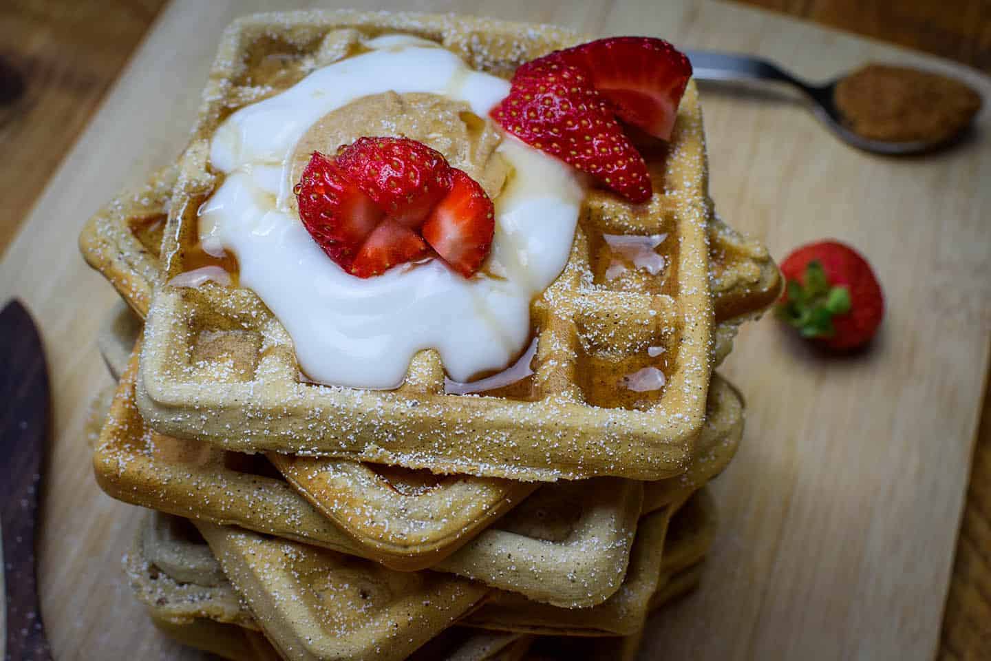 Close up of a stack of waffles from above that are loaded with strawberries, coconut yoghurt and peanut butter