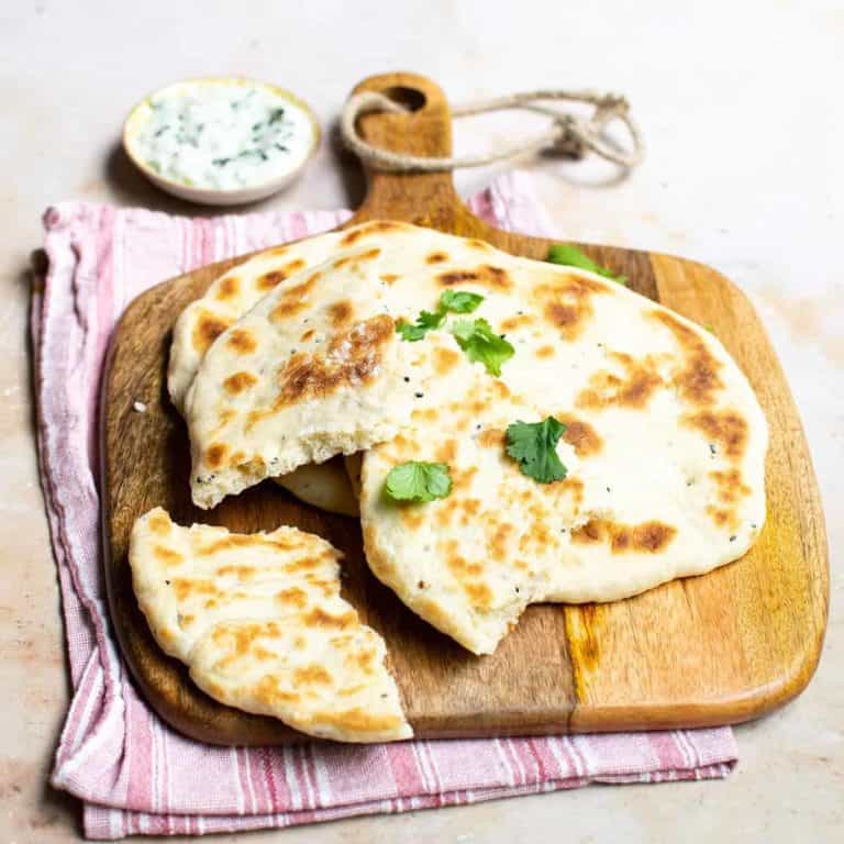 Vegan naan bread on a wooden chopping board with raita in the background