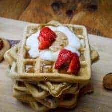 simple vegan waffles stacked up. Birds eye view of strawberries, coconut yoghurt and peanut butter.There's a spoon in the background with sugar on it.