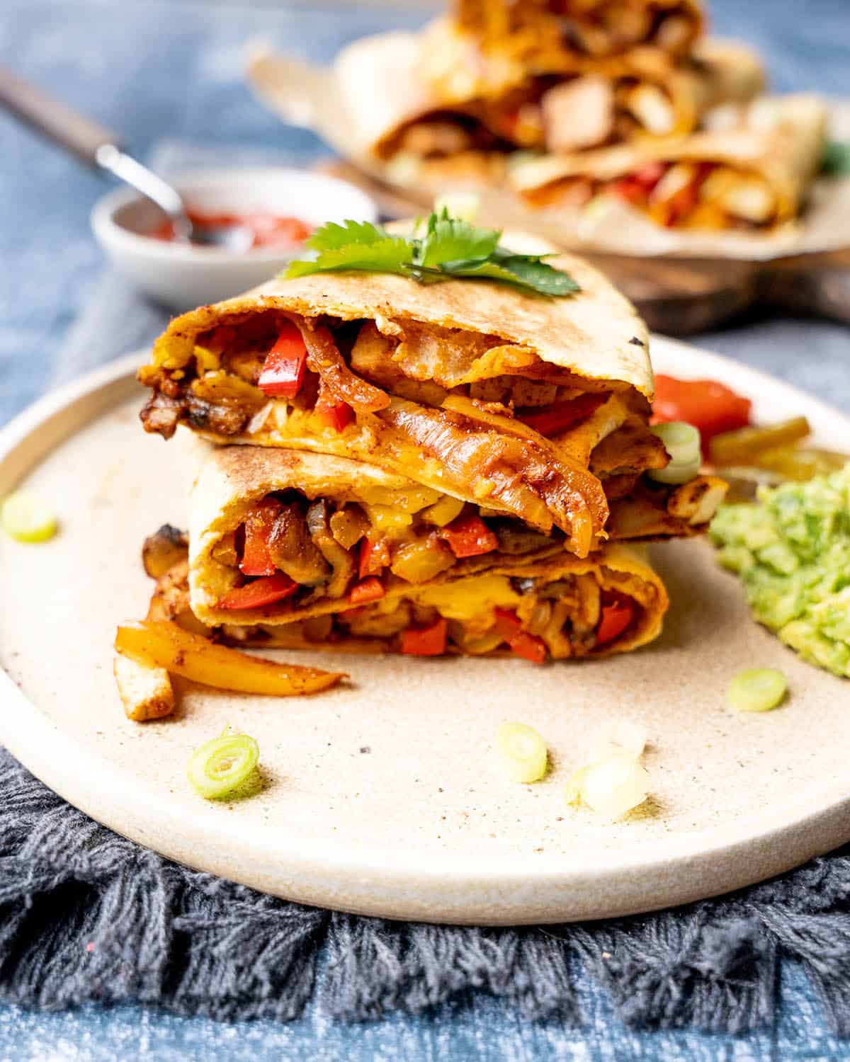 Three pieces of tofu quesadilla with mushrooms and peppers in a stack on a plate.