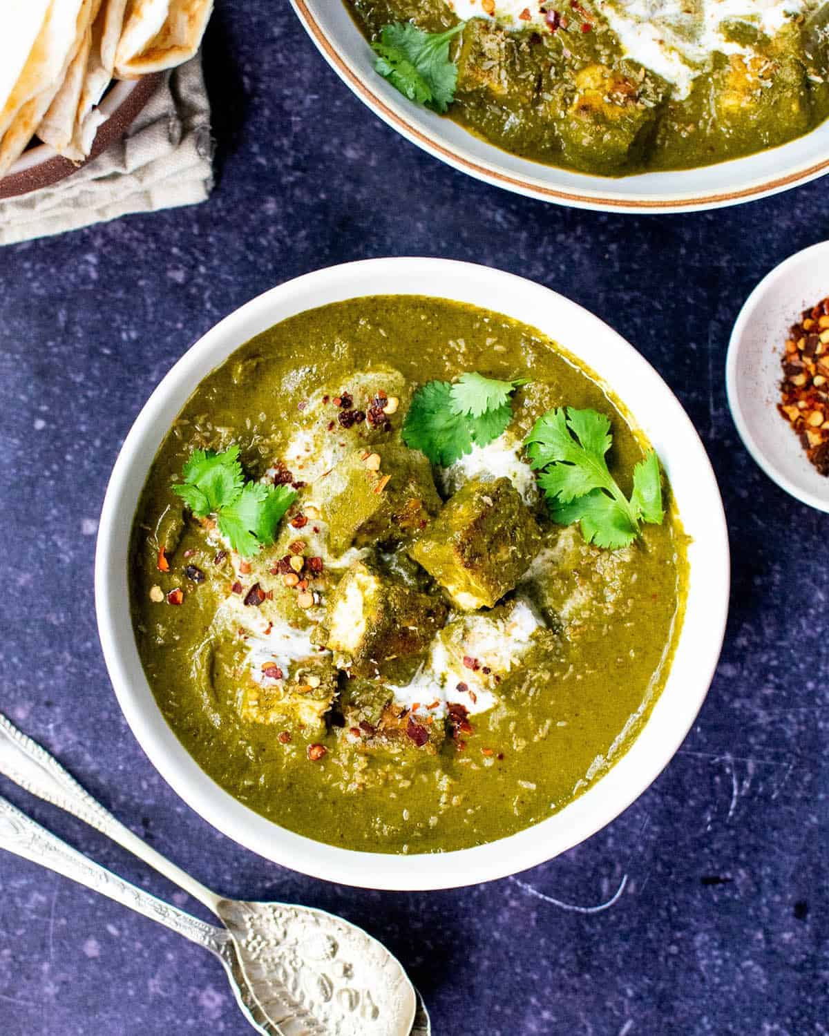 A bowl of vegan palak paneer with tofu laying on top of the green gravy.