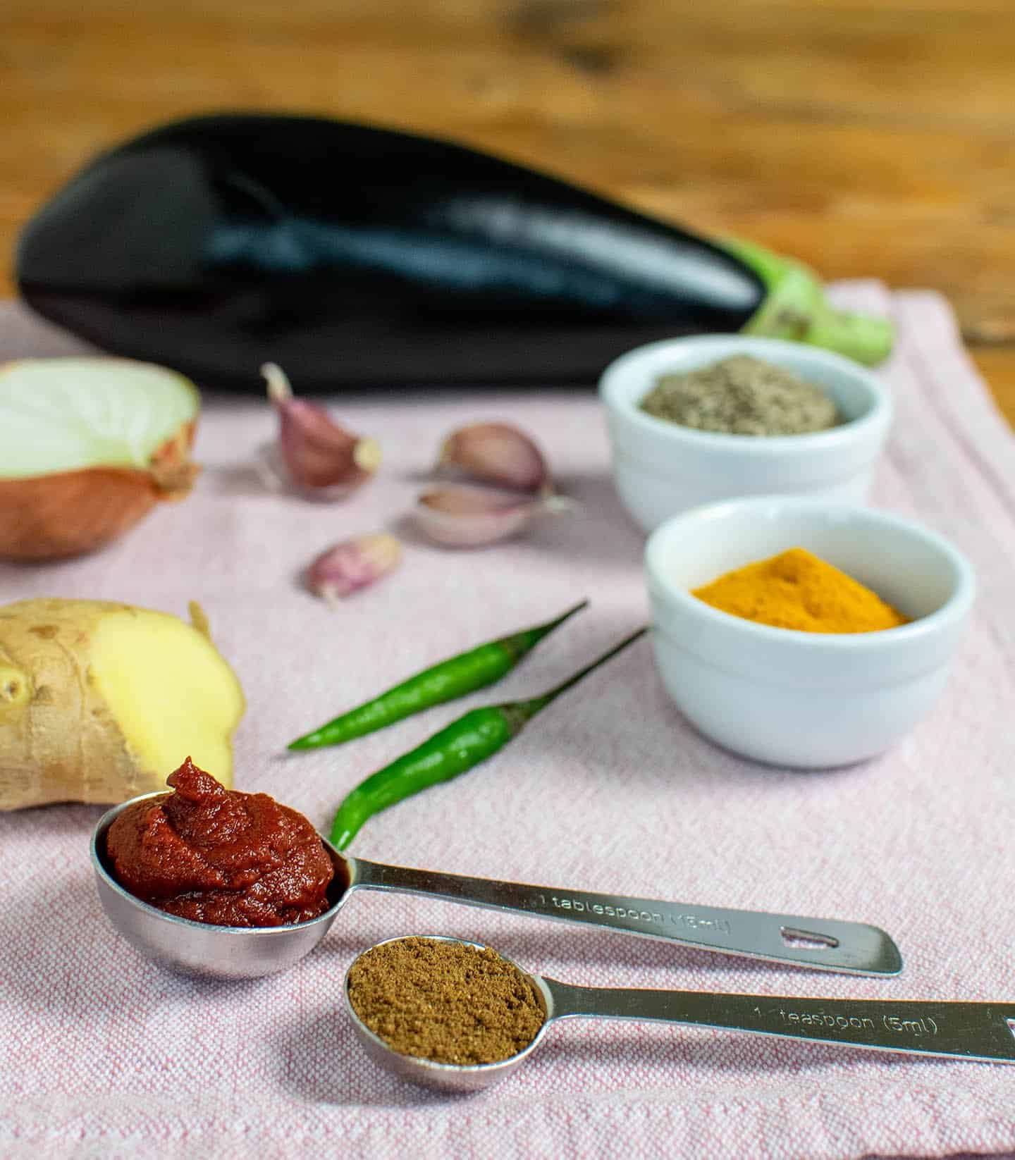 Ingredients laid out on a pink tea towel. It shows chillies, spices, ginger, aubergine and tomato puree