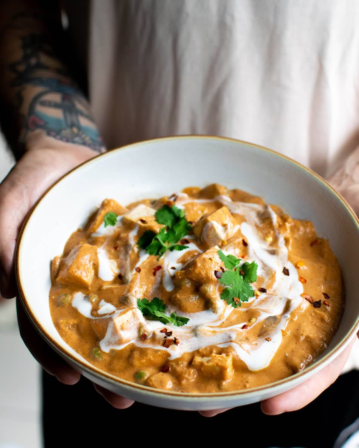 A man holding a bowl of vegan butter chicken, topped with fresh coriander