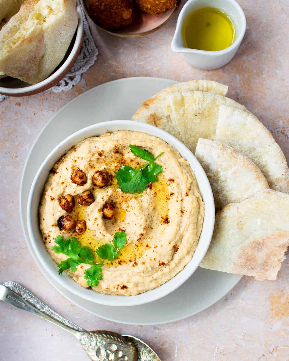 Lebanese hummus in a white bowl with pitta bread, olive oil and falafels nearby