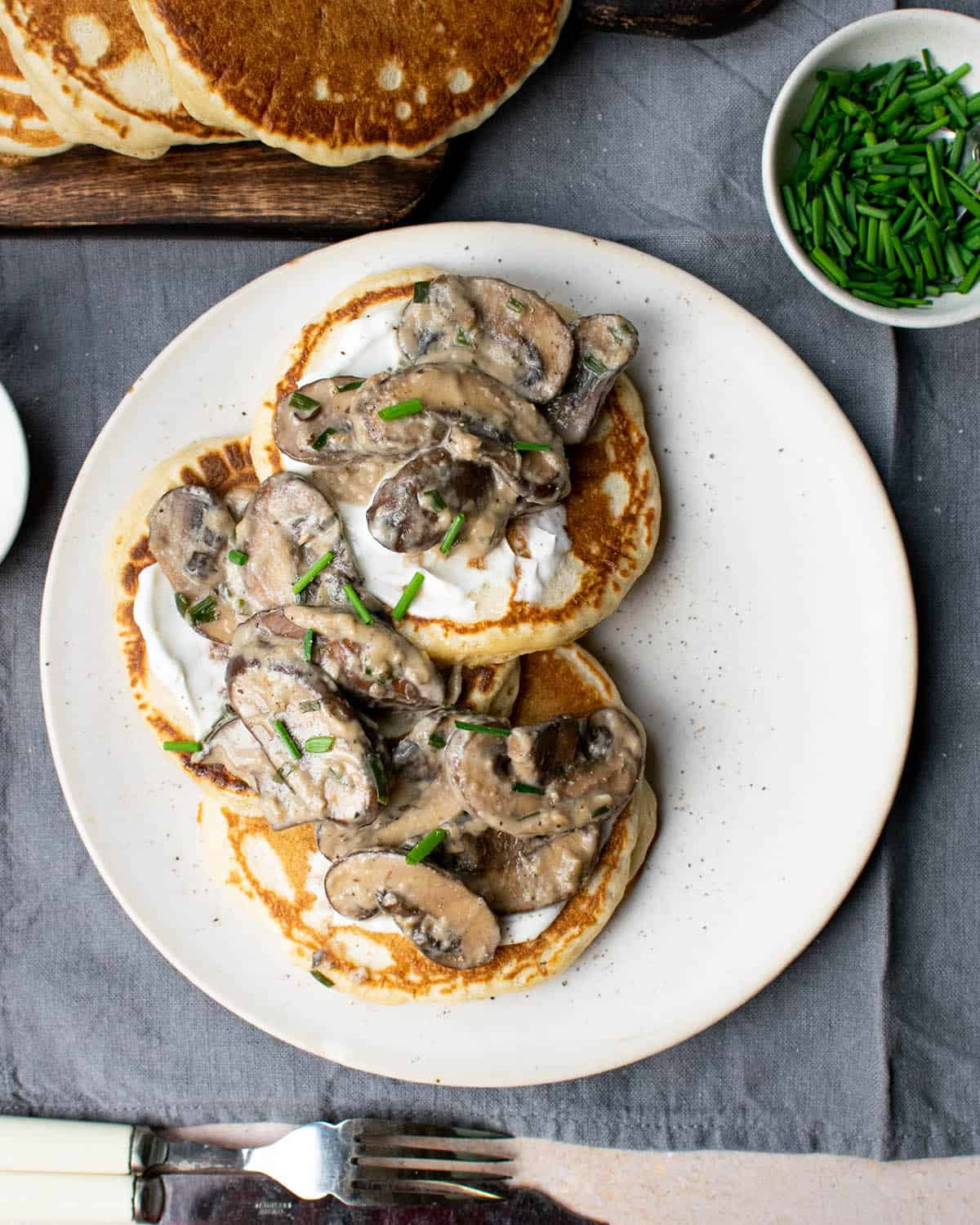 Top down view of vegan savoury pancakes on a plate topped with mushrooms and chives.