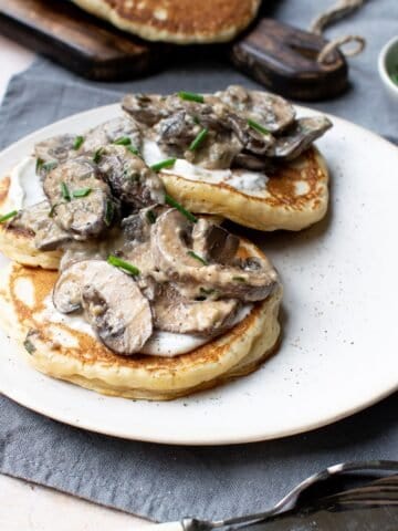 Side view of three pancakes on a plate topped with mushrooms and vegan creme fraîche.