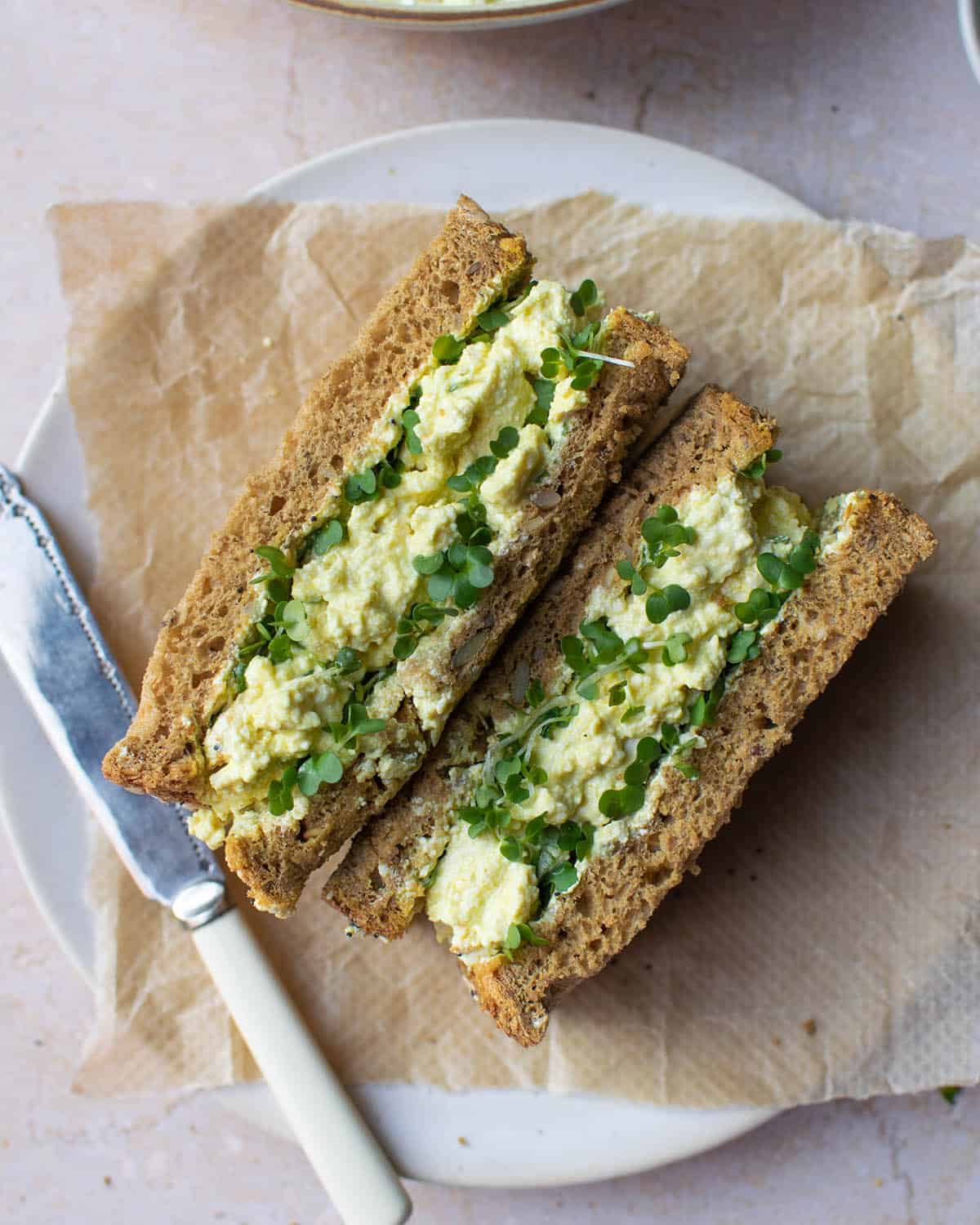 Top down view of vegan egg mayo sandwich on a plate with a knife